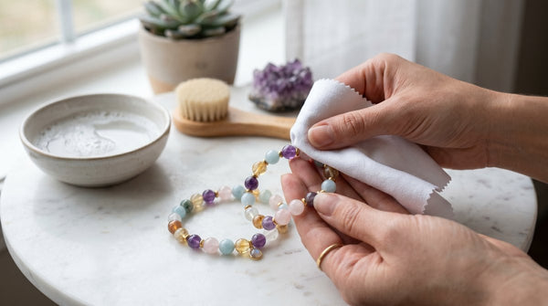 A person gently cleaning a gemstone bead bracelet with a soft cloth on a marble table