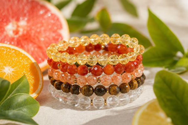 Stack of crystal bracelets in warm summer sunlight with citrus and green leaves