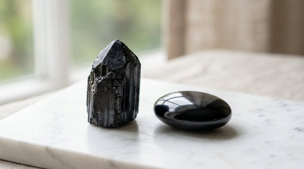 Black tourmaline crystal and polished black obsidian stone on marble surface