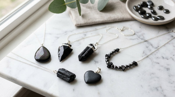 Black tourmaline, obsidian, hematite, and shungite protection crystal pendants on silver chains on marble surface